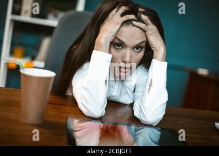 Gestresste Geschäftsfrau fühlt emotionalen Stress. Gelangweilte oder verrückte Frau, die am Arbeitsplatz mit einer Kaffeetasse in Stupor fällt. Krisenkonzept. Getöntes Bild Stockfoto