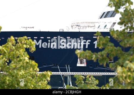 1. August 2020, Kiel, mit Mein Schiff 1 der Reederei TUI Cruises hat das erste Kreuzfahrtschiff nach Ausbruch der Coronapandemie im Hafen von Kiel am Ostseekai vertäut. Detail des Bogens mit dem Namen des Schiffes durch die Bäume am Terminal. Weltweite Nutzung Stockfoto