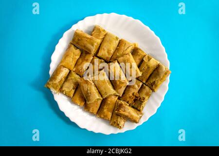 Traditionelle türkische, arabische, mittelöstliche Baklava. Draufsicht. Arabisch gebackene Süßigkeiten in weißem Teller auf blauem hellen Hintergrund. Mini Baklawa Stockfoto