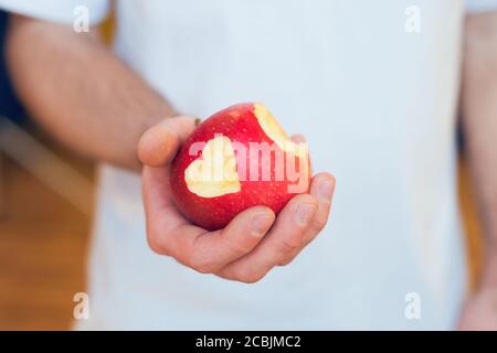Gebissen roten Apfel mit geschnittenen Herzen in der männlichen Hand Stockfoto