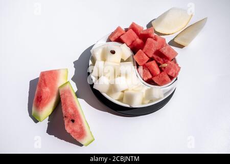 Reife Wassermelone und Melone gewürfelt und in Scheiben geschnitten. Auf einer Yin Yang-förmigen Schale auf weißem Hintergrund ausgelegt. Saftige, reife Sommerfrüchte. Speicherplatz kopieren. Stockfoto