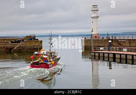 Newhaven Harbour, Edinburgh, Schottland, Großbritannien. 14. August 2020. Temperatur 17 Grad und stark bewölktes Wetter, als das Carrie B Fischerboot zur Arbeit in den Firth of Forth mit dem Leuchtturm auf der rechten Seite des kleinen Hafens aufbrechen wird. Erst heute Morgen berichteten die Gesundheitsbehörden in Orkney, dass sie es mit einer Gruppe von fünf bestätigten Covid-19-Fällen zu tun haben, die mit einem Fischerboot in Verbindung stehen. Stockfoto