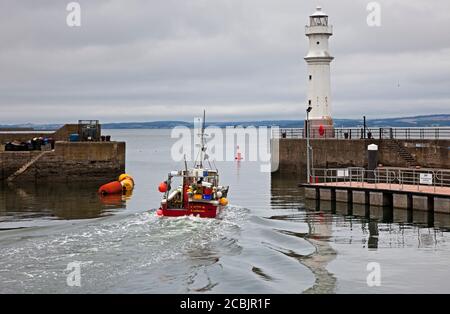 Newhaven Harbour, Edinburgh, Schottland, Großbritannien. 14. August 2020. Temperatur 17 Grad und stark bewölktes Wetter, als das Carrie B Fischerboot zur Arbeit in den Firth of Forth mit dem Leuchtturm auf der rechten Seite des kleinen Hafens aufbrechen wird. Erst heute Morgen berichteten die Gesundheitsbehörden in Orkney, dass sie es mit einer Gruppe von fünf bestätigten Covid-19-Fällen zu tun haben, die mit einem Fischerboot in Verbindung stehen. Stockfoto