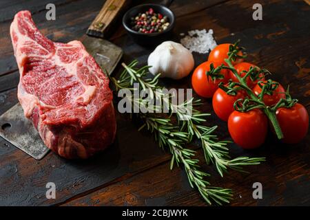 Rohes Cowboy Steak auf Fleischspalter. Bio-Bauernhof marmorierte Prime schwarz angus Rindfleisch. Dunkler Holzhintergrund. Seitenansicht. Mit Gewürzen, Pfefferkörnern, Chilischoten Stockfoto