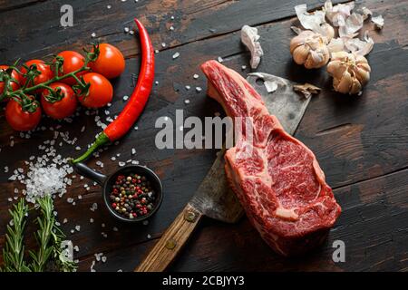 Rohes trockenes Delmonico Steak auf dunklem Holz Vintage Tisch Hintergrund. Spencer Steak oder Beauty Steak BBQ mit Gewürzen, Rosmarin, Tomate, Chikie, Knoblauch Stockfoto