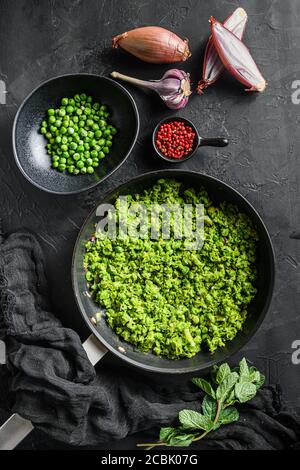 Mushy Erbsen Rezept gekochte Pfanne und Erbsen in der Schüssel Mit Minze Schalotte Pfeffer und Salz über schwarzer Steinoberfläche Draufsicht Bio-Keto Lebensmittel flach legen Stockfoto