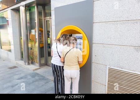 Huelva, Spanien - 13. August 2020: Nicht identifizierte Frauen, die eine Bankkreditkarte in einem Geldautomaten verwenden, tragen eine Schutzmaske wegen Covid-19 coronaviru Stockfoto