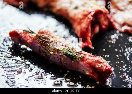 Lammfleisch bbq Zubereitung. Nahaufnahme von Lammkoteletts mit Gewürzen und Rosmarin auf schwarzem rustikalem Teller. Restaurant Küche Grillgericht. Stockfoto