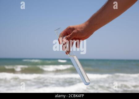 Reagenzglas mit sauberem Meerwasser in einer Hand auf Ein Meereshintergrund während ökologischer Prüfung Stockfoto