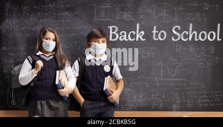 Schulmädchen und Schuljunge mit Schutzmasken stehen vor Eine Schultafel mit Text zurück zur Schule Stockfoto