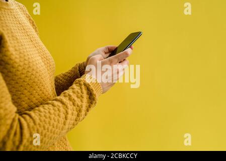 Frau in gelben Pullover mit Smartphone in den Händen Stockfoto