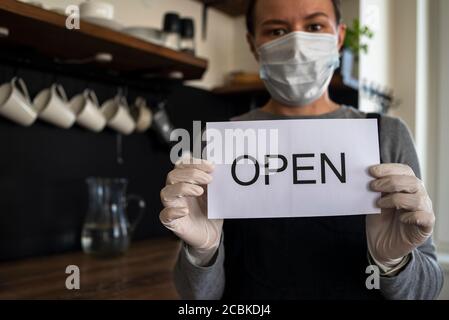 Kellnerin mit OFFENEM Schild in Gesichtsmaske und Handschuhen. Nach der Sperre wieder öffnen Stockfoto