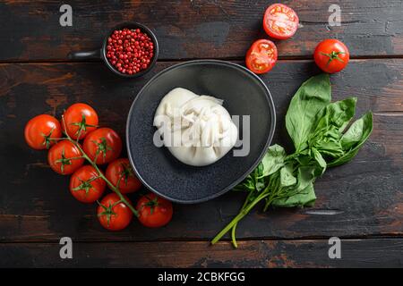Burrata Handmade Cheese Schwarzer Teller serviert mit frischen rohen Tomaten und Basilikumblättern, flachliegend auf dunklem Holzhintergrund, horizontal geschossen Stockfoto