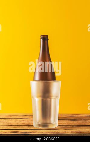 Leeres Bierglas, Flaschenbier auf Holzhintergrund und gelber, selektiver Fokus. Stockfoto