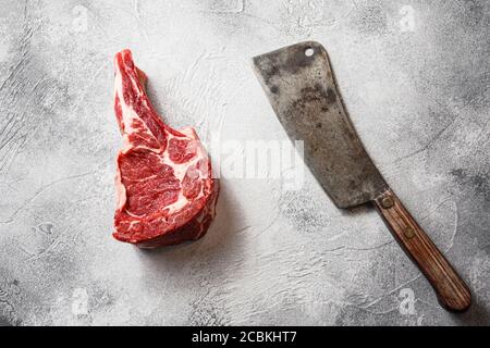 Rohe schwarze angus Rindfleisch Tomahawk Steaks auf Knochen in der Nähe der Fleisch american Spaltmesser über grauen Stein Tisch Schiefer Schneiden Draufsicht Stockfoto