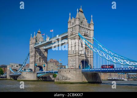 England, London, Tower Bridge Blick vom Südufer der Themse mit einem ikonischen roten Londoner Bus, der die Brücke überquert. Stockfoto