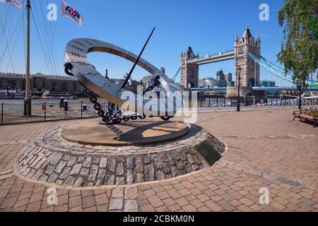 England, London, St Katherine’s Dock , Blick auf die Tower Bridge mit der Uhrmacherskulptur, die einer Sonnenuhr ähnelt, die Wendy Taylor 1973 schuf. Stockfoto