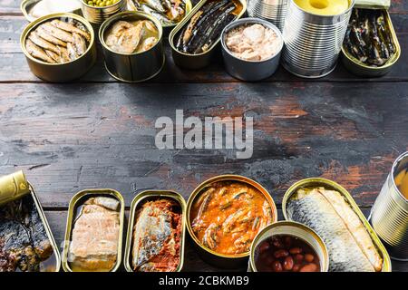 Platz für Text zwischen zwei Zeilen aus verschiedenen Konserven zubereitetes Gemüse, Fleisch, Fisch und Obst in Dosen. Auf einem hölzernen Hintergrund Seitenansicht Stockfoto