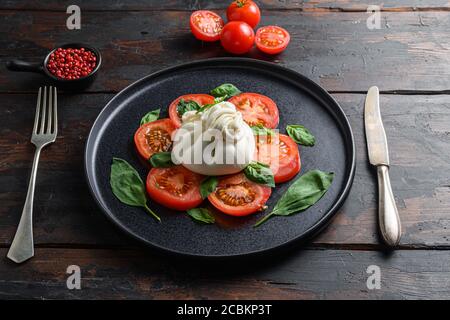 Cremiger italienischer Burrata-Käse, serviert mit Olivenöl und Basilikum Blätter auf schwarzem Teller über altem Holztisch Stockfoto