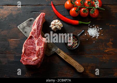 Rohes Ribeye Steak auf Fleischspalter. Bio-Bauernhof marmorierte Prime schwarz angus Rindfleisch. Dunkler Holzhintergrund. Draufsicht. Mit Gewürzen, Pfefferkörnern Stockfoto