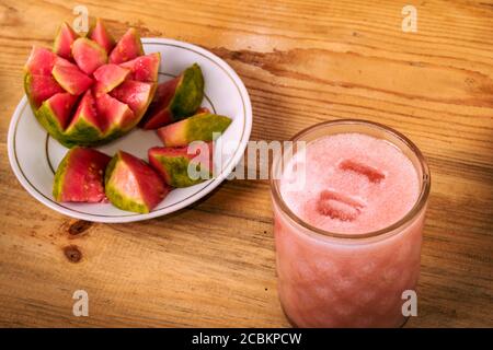 Foto eines kalten Guava-Saftes in einem Kristallglas mit einer Schale mit Guava-Scheiben darauf in der Nähe, alles auf einem Holztisch. Stockfoto