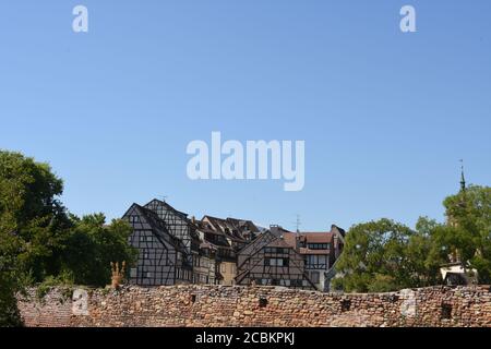 Fachwerkgebäude aus dem Mittelalter und der Frührenaissance hinter roten Ziegelmauern unter blauem Himmel in Colmar, einer Stadt in der Region Grand Est in Frankreich. Stockfoto