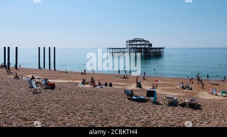 Brighton and Hove, E Sussex, UK - August 2020: Menschen im Meer und am Strand in der Nähe des West Pier. Stockfoto