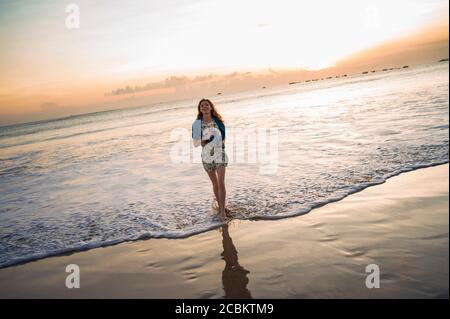 Mittlere Erwachsene Frau, die bei Sonnenuntergang im Meer spazieren geht, Jimbaran Bay, Bali, Indonesien Stockfoto