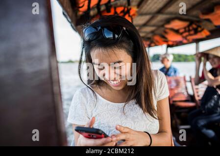 Frau, die auf Foto im Mobiltelefon auf dem Kreuzfahrtschiff, Mekong Delta, Vietnam Stockfoto