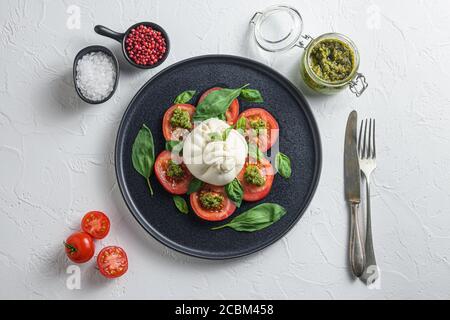 Salat mit traditionellem italienischen Burrata-Käse aus Sahne und Büffelmilch oder Kuhmilch mit Pesto und Tomaten und Gewürze auf schwarzem flachen Teller Stockfoto