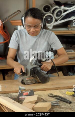 Austin, Texas, USA, 1996: Afroamerikanische Frau benutzt elektrischen Bandschleifer, während sie Schutzbrillen und Ohrbeläge trägt. Model Veröffentlicht ©Bob Daemmrich Stockfoto