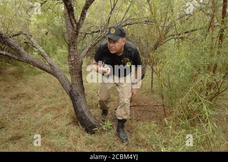 Los Indio, Texas USA, 12. September 2006: Cursti Collier aus Houston duckt unter einem Mesquite-Baum, als er und andere Mitglieder der Texas Minutemen Ranchland im Maverick County etwa 1/2 Meilen von der texanischen Grenze zu Mexiko patrouillieren. Die Mitglieder haben eine zweimonatige Operation begonnen, um Grundbesitzer bei der Sicherung privater Ranches entlang der 700 Meilen langen Grenze von Texas zu Mexiko zu unterstützen. ©Bob Daemmrich Stockfoto