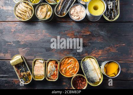 Platz für Text zwischen zwei Zeilen aus verschiedenen Konserven zubereitetes Gemüse, Fleisch, Fisch und Obst in Dosen. Auf einem hölzernen Hintergrund Draufsicht Stockfoto