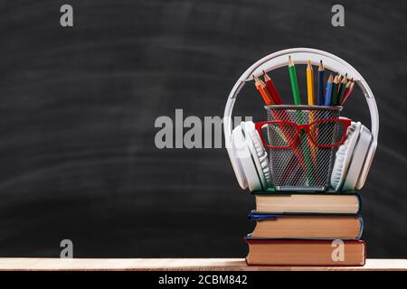 Zurück zur Schule. Komposition aus einem Stapel von Büchern Bleistifte Brille Kopfhörer auf einem schwarzen Kreidetafel Hintergrund. Tag des Lehrers. Stockfoto