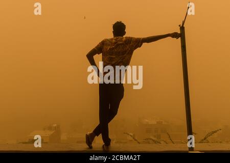 Erwachsener Mann, der sich mitten im Sandsturm an der Stange lehnte, der Mann genießt es, während des Sandsturms der Stadt gegenüber zu sein Stockfoto