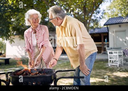 Glückliches Seniorenpaar bereitet Grill im Garten zusammen. Stockfoto