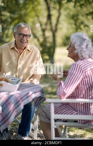 Lächelndes Seniorenpaar genießt gemeinsam draußen und trinkt Kaffee. Stockfoto