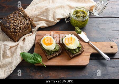 Frisches grünes Basilikum Pesto im Glas hausgemachte auf alt Rustikale Holzeier Panini Brot mit Pesto und heißem sriracha Sauce italienisches Frühstück mit Stockfoto