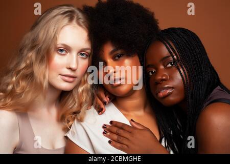 Junge hübsche kaukasische, afro, skandinavische Frau posiert fröhlich zusammen auf braunem Hintergrund, Lifestyle diverse Nationalität Menschen Konzept Stockfoto
