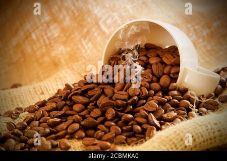 Nahaufnahme verschütteter Kaffeebohnen aus einer weißen Tasse Ein Sacktuch Stockfoto