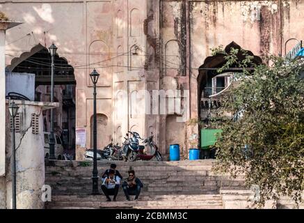 Bhopal, Madhya Pradesh, Indien - März 2019: Junge indische Jungen sitzen auf den Stufen, die das alte gewölbte Tor von Shaukat Mahal führen. Stockfoto