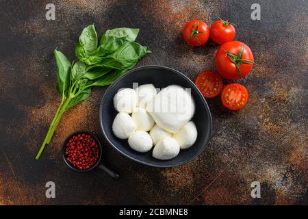 Leckere Mozzarella Käse mit Basilikum und Tomaten in schwarzer Schüssel, Zutaten für Salat Caprese. Auf alten rustikalen Metall-Hintergrund. Caprese Salat Stockfoto