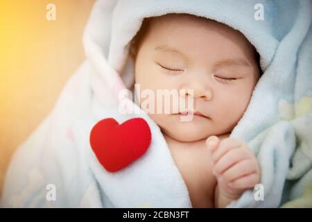 Familie Liebe Beziehung Konzept : rotes Herz geformt setzen auf Schlaf niedlich asiatische Baby. Schöne neugeborene Asien Kleinkind Modell weiblich in ihrem ersten Jahr Stockfoto