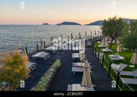 Hochwinkelansicht eines leeren touristischen Resorts mit Sonnenliegen und Sonnenschirmen am Ufer des Golfes der Dichter bei Sonnenuntergang, San Terenzo, La Spezia, Italien Stockfoto