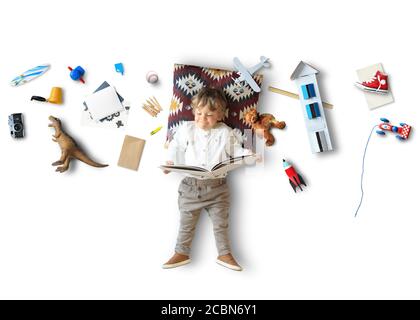 Kleiner Junge lügt und liest ein Buch unter seinen Spielsachen Stockfoto