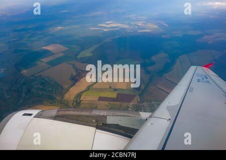 Blick vom Flugzeug-Illuminator. Der Blick aus dem Fenster des Flugzeugs auf den Flügel, die Erde und die Felder. Stockfoto