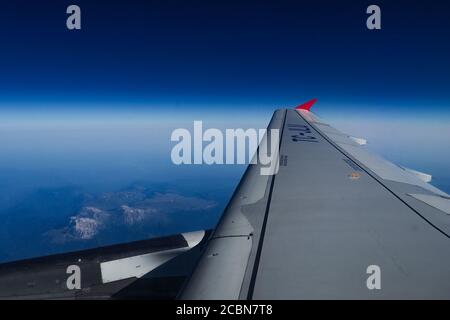 Blick vom Flugzeug-Illuminator. Der Blick aus dem Fenster des Flugzeugs auf den Flügel, die Berge und den blauen Himmel Stockfoto