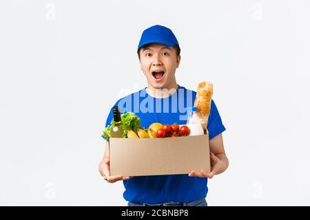 Online-Shopping, Lebensmittelzustellung und Versandkonzept. Staunend lächelnd junge asiatische männliche Kurier, in Uniform und Übergabe Box mit frischen Lebensmitteln zu Stockfoto