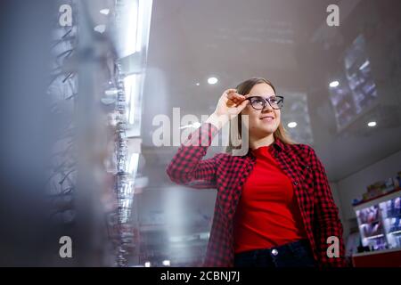 Ein sehbehindertes Mädchen wählt eine Brille. Sie trägt ein Hemd und ein schönes Lächeln. Stockfoto