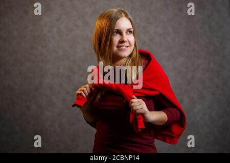 Mädchen versucht auf einem roten Pullover auf einem grauen Hintergrund Stockfoto